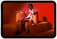 Vista frontal de un iPad mini que muestra una imagen nítida de una persona con un traje naranja sentada en una silla naranja en una habitación naranja