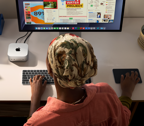 Una persona escribe en un escritorio que tiene una Mac mini, un monitor Studio Display conectado, un Magic Keyboard, un Magic Trackpad, varios artículos