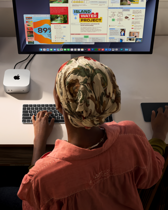 Una persona escribe en un escritorio que tiene una Mac mini, un monitor Studio Display conectado, un Magic Keyboard, un Magic Trackpad, varios artículos