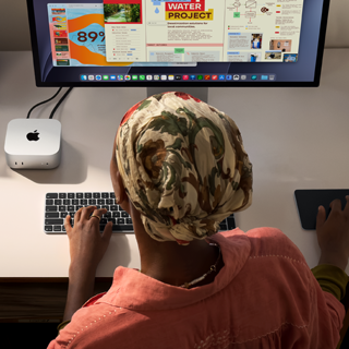Una persona escribe en un escritorio que tiene una Mac mini, un monitor Studio Display conectado, un Magic Keyboard, un Magic Trackpad, varios artículos