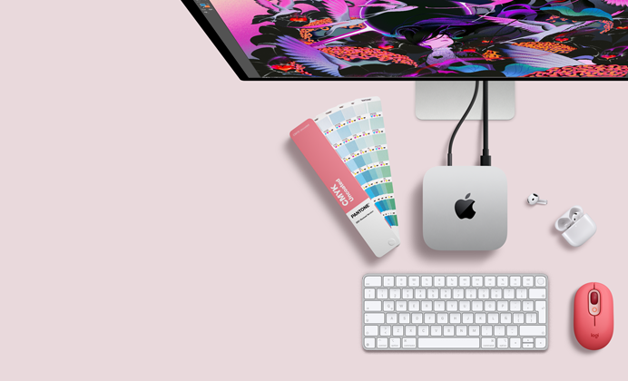 Mac mini, parte superior, aluminio color plata, esquinas redondeadas, logo de Apple en el centro en color negro brillante, conectada con un cable, monitor Studio Display parcialmente visible en la parte superior, AirPods 4, abiertos, muestra de una paleta de colores Pantone, teclado numérico y mouse