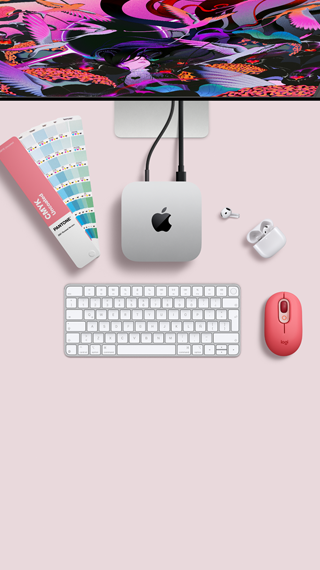 Mac mini, parte superior, aluminio color plata, esquinas redondeadas, logo de Apple en el centro en color negro brillante, conectada con un cable, monitor Studio Display parcialmente visible en la parte superior, AirPods 4, abiertos, muestra de una paleta de colores Pantone, teclado numérico y mouse