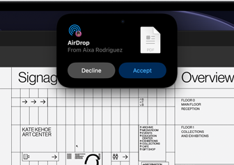 Una pantalla muestra la Dynamic Island con una solicitud de AirDrop en una ventana pequeña sobre un archivo de Adobe Acrobat abierto