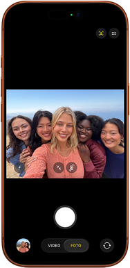 iPhone 17 Pro en naranja cósmico, frente, la pantalla muestra la cámara frontal Center Stage abierta con una selfie grupal de cinco personas centradas en el encuadre
