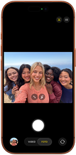 iPhone 17 Pro en naranja cósmico, frente, la pantalla muestra la cámara frontal Center Stage abierta con una selfie grupal de cinco personas centradas en el encuadre